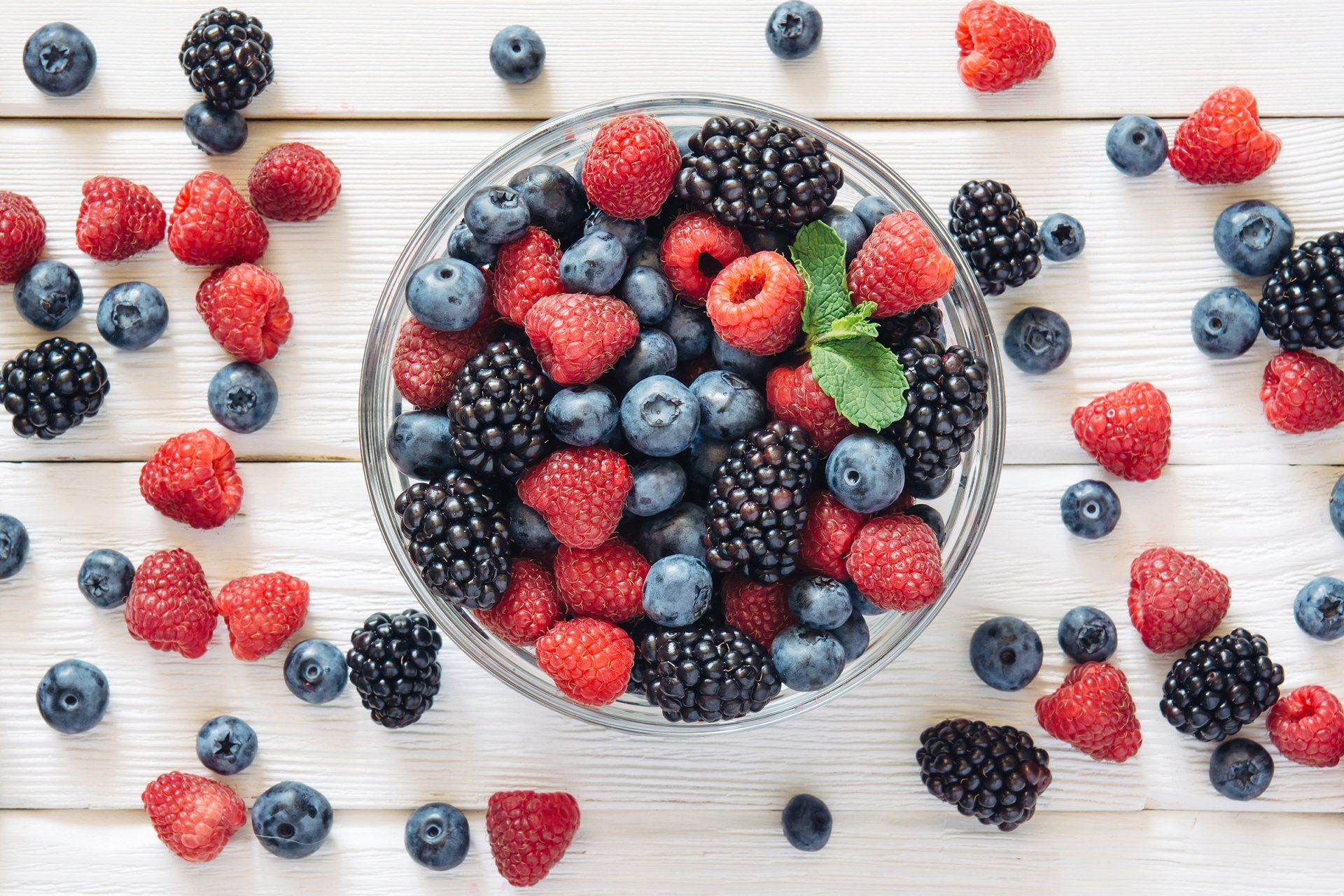 Bowl of mixed berries (blueberries, raspberries, blackberries) on a white wooden surface.