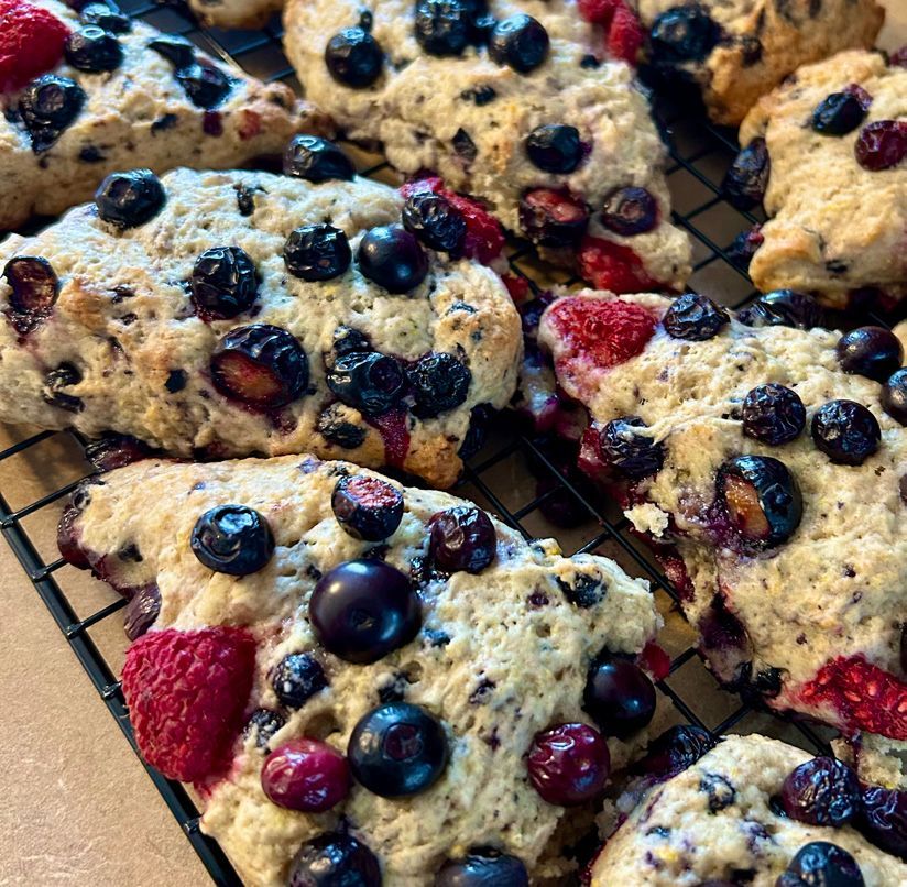 Close-up of baked blueberry and raspberry scones cooling on a black wire rack. The scones are golden brown with visible fruit.