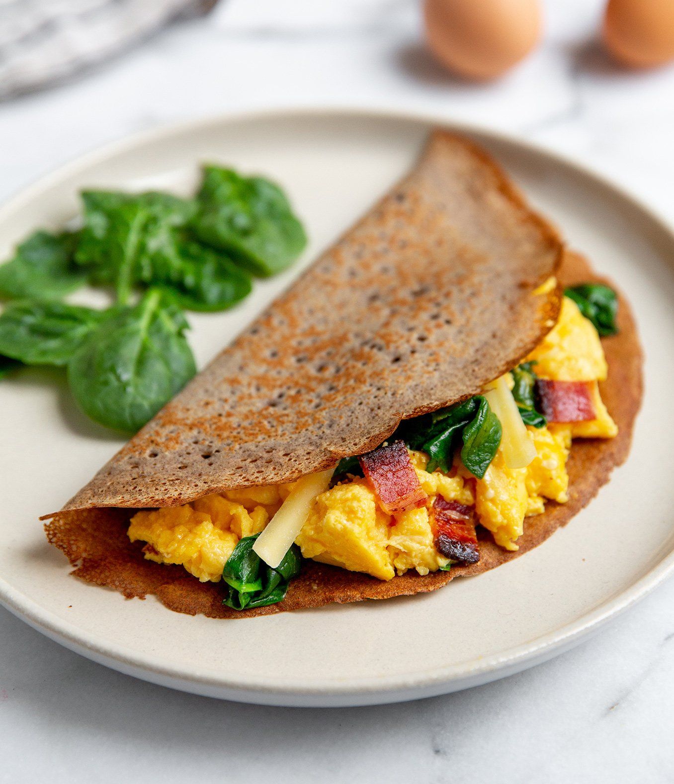 Breakfast crepe filled with scrambled eggs, bacon, spinach, and cheese; side of spinach.