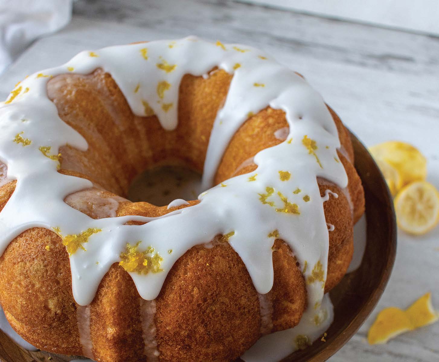 Lemon Bundt cake with white glaze and lemon zest garnish on a wooden plate.