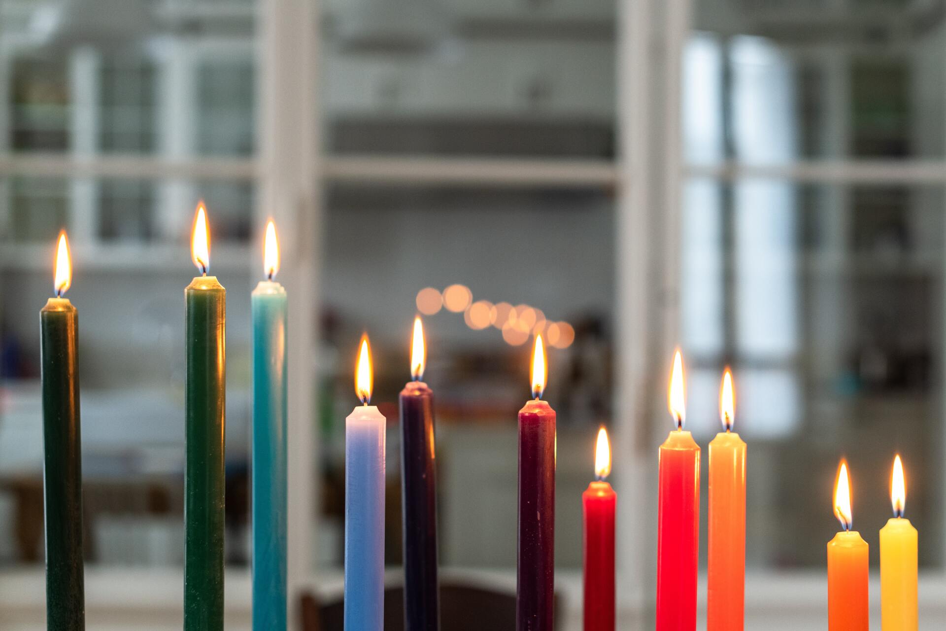 A colorful menorah with lit candles, in front of a window with out-of-focus lights.