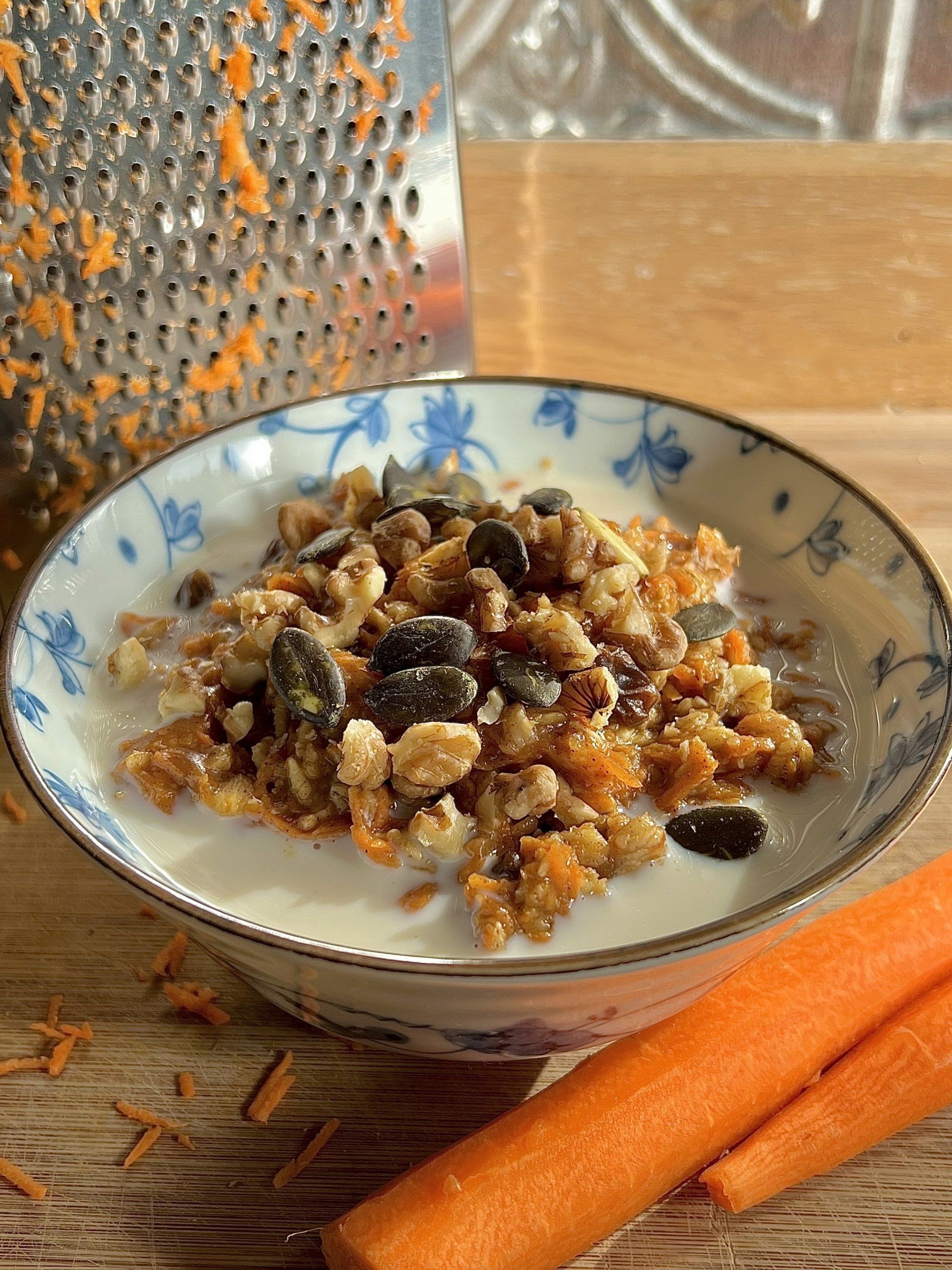 A bowl of granola in milk, with a carrot and grater visible.