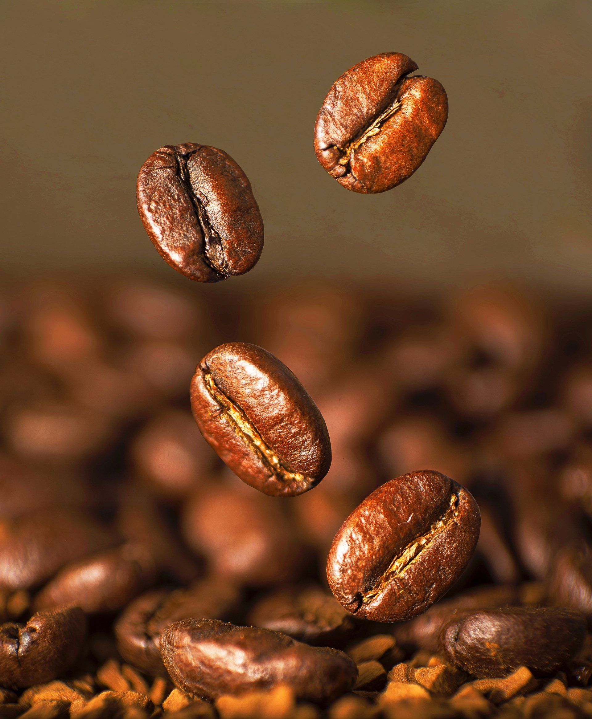 Close-up of roasted coffee beans, with four beans floating in the air above a pile of coffee grounds and beans.