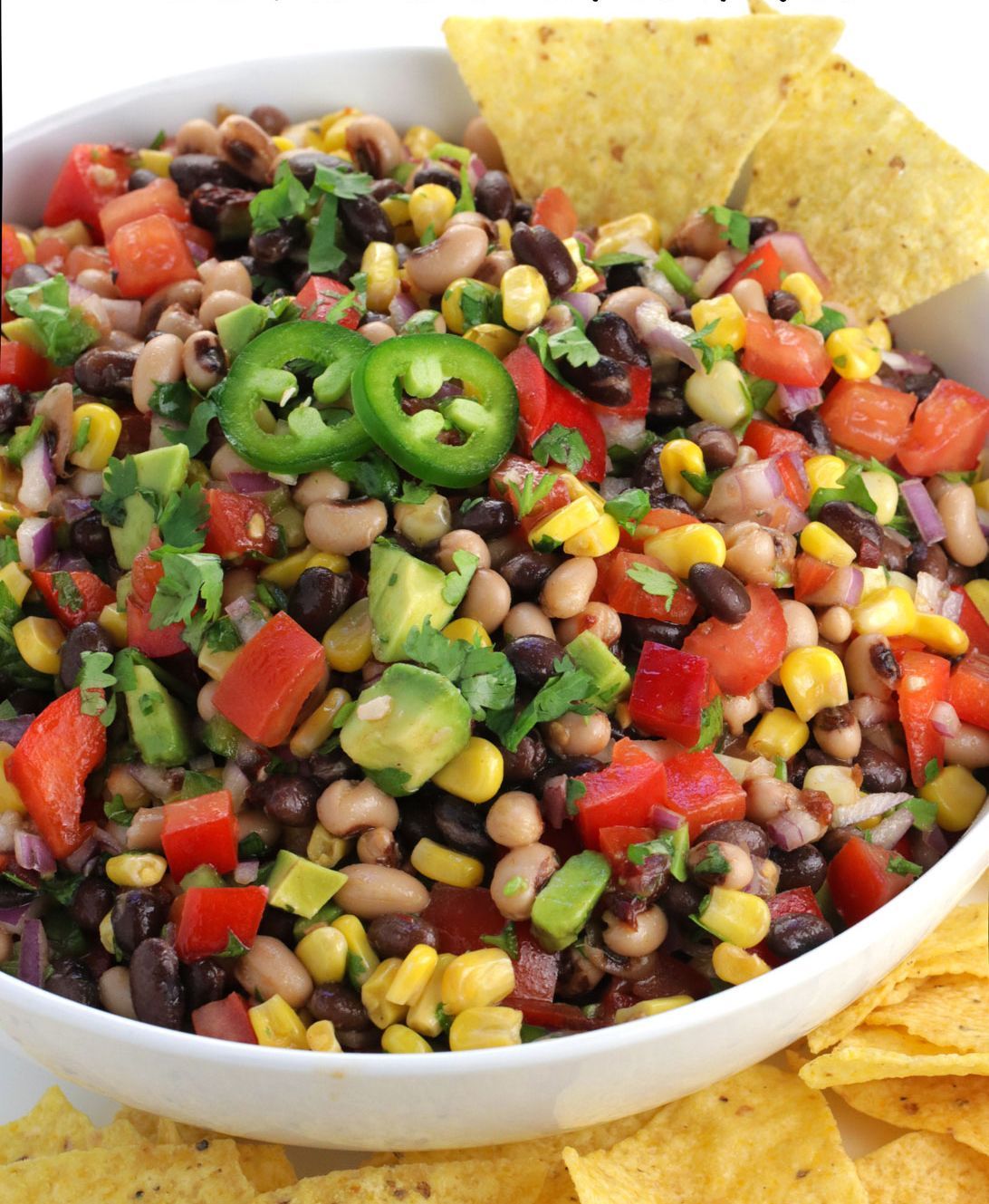 Bowl of black bean and corn salsa with avocado, tomatoes, and jalapeños; served with tortilla chips.