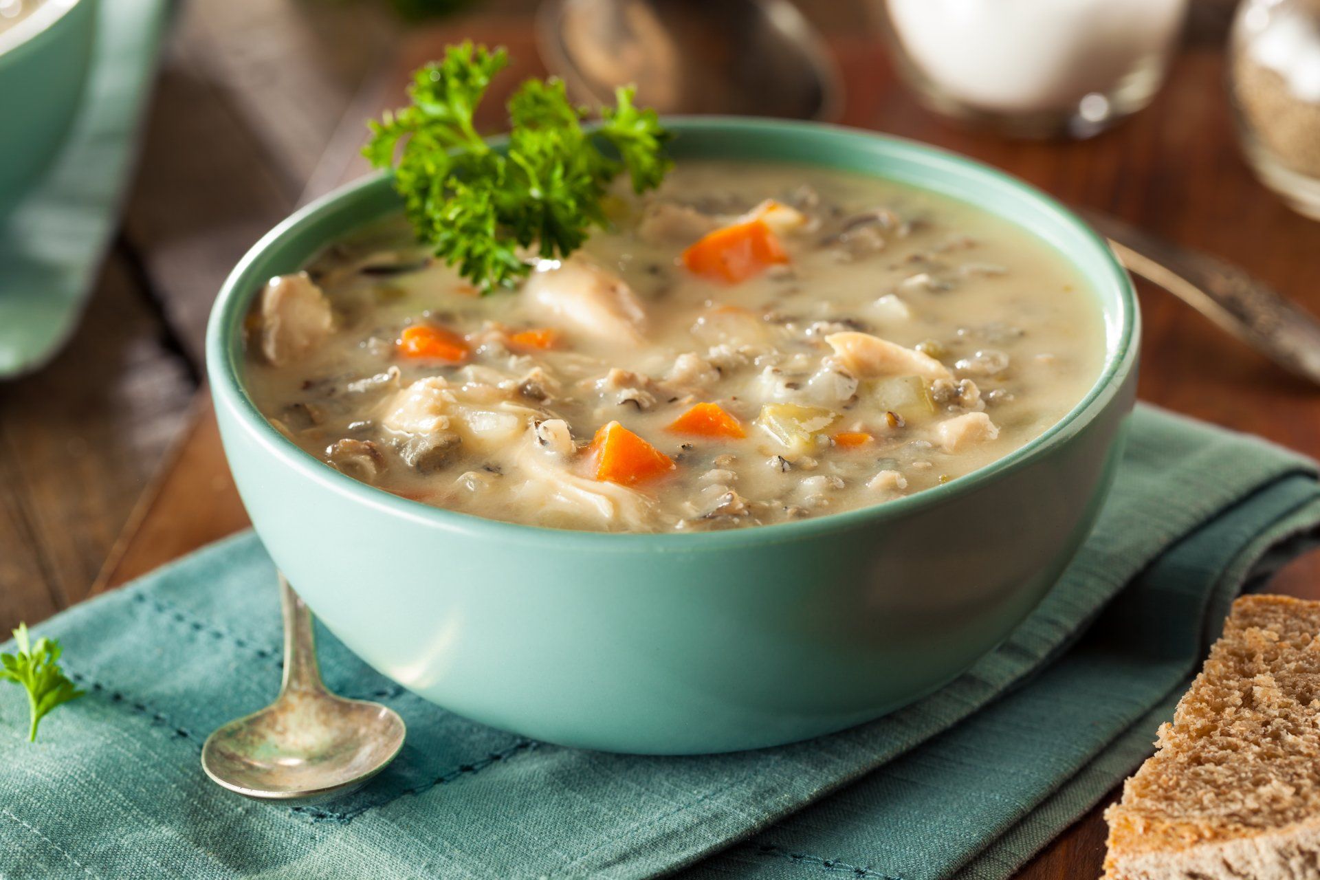 Bowl of creamy chicken and wild rice soup with carrots, parsley garnish, and bread.