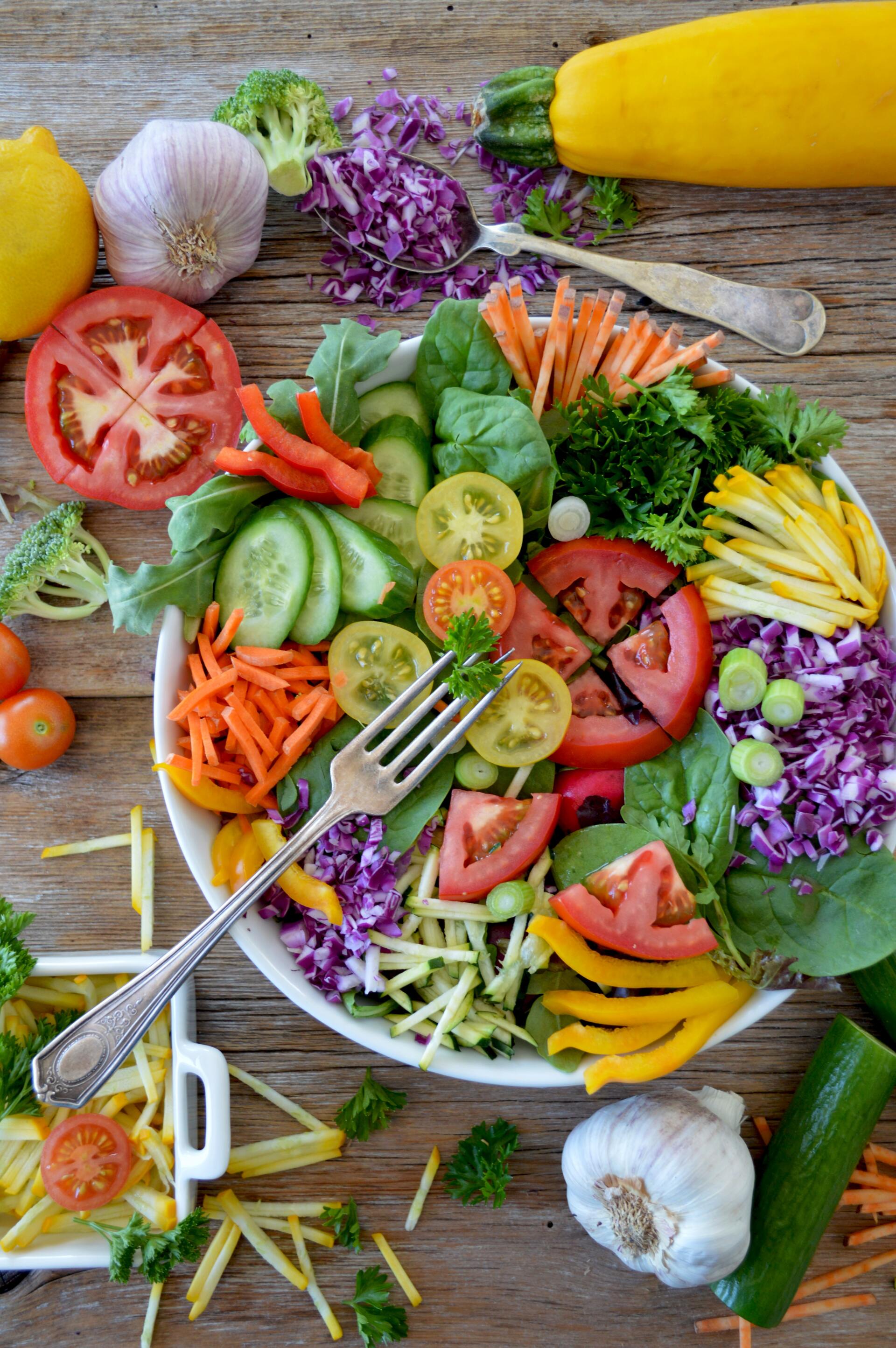 Vibrant salad bowl with various colorful vegetables like tomatoes, carrots, and cabbage, on a wooden surface. A fork is resting in the salad.