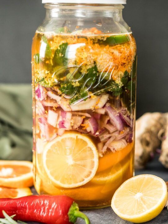 Jar of fermenting vegetables and fruit, including lemons, red onions, and chilies.