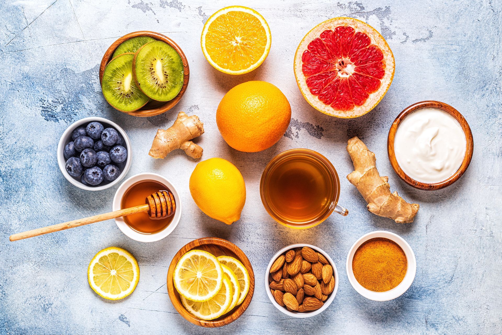 Overhead shot of various foods known for immunity, including fruits, ginger, honey, and nuts. The foods are arranged on a blue and white surface.