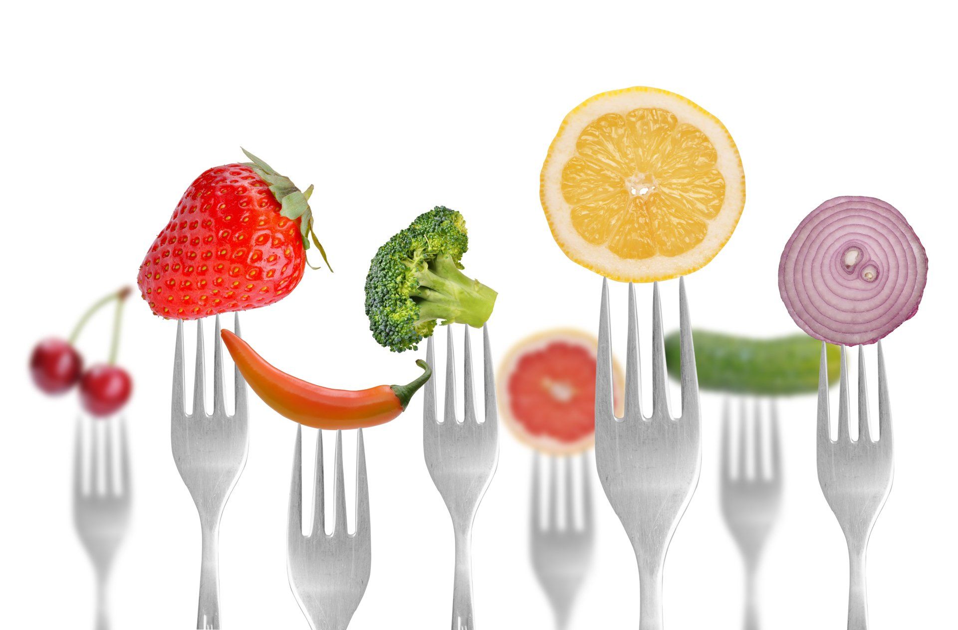 Various fruits and vegetables impaled on forks against a white background. Includes a strawberry, broccoli, lemon, and onion.