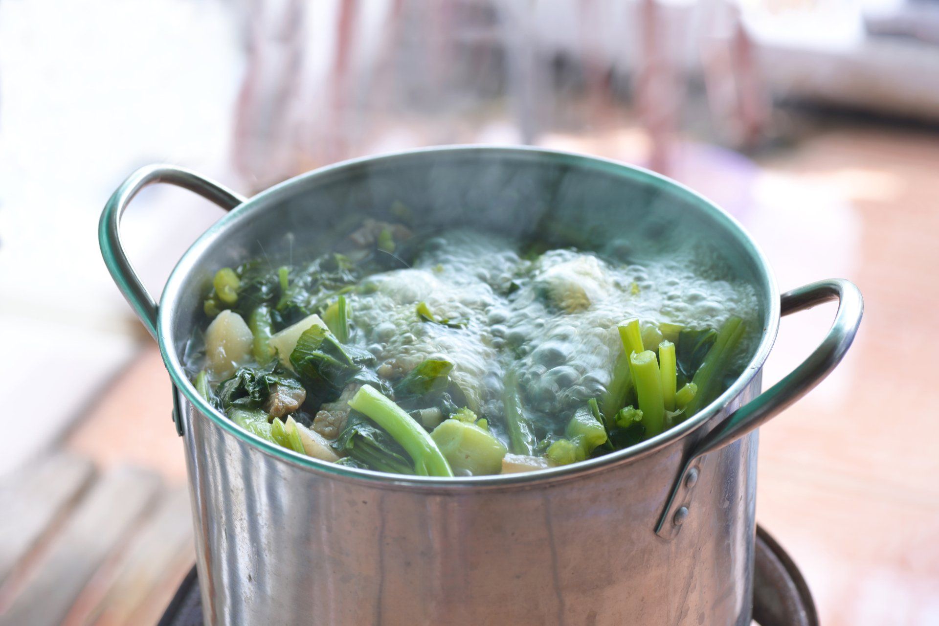 A pot of boiling green vegetables, steam rising. Silver pot with black handles sits on a burner.