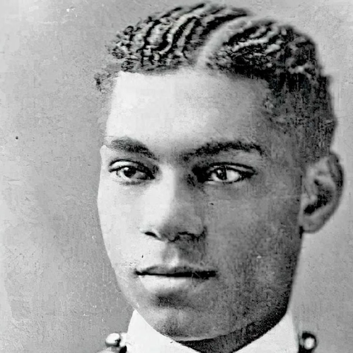 Young Black man with short, wavy hair, looking towards the camera. He wears a formal collared shirt.