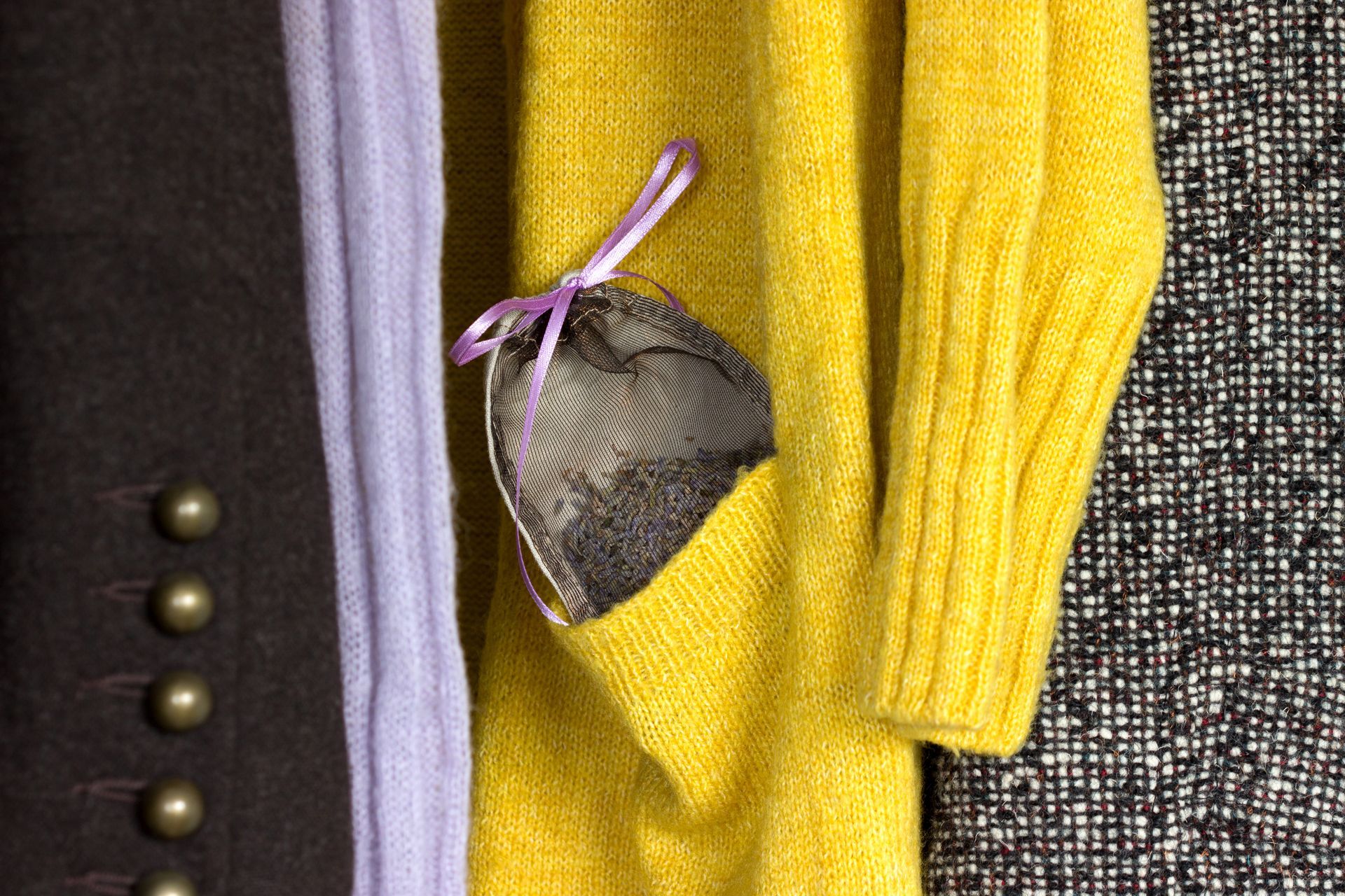 A yellow sweater with a pocket holding a gray mesh bag tied with a purple ribbon. Adjacent are brown and black clothing items.