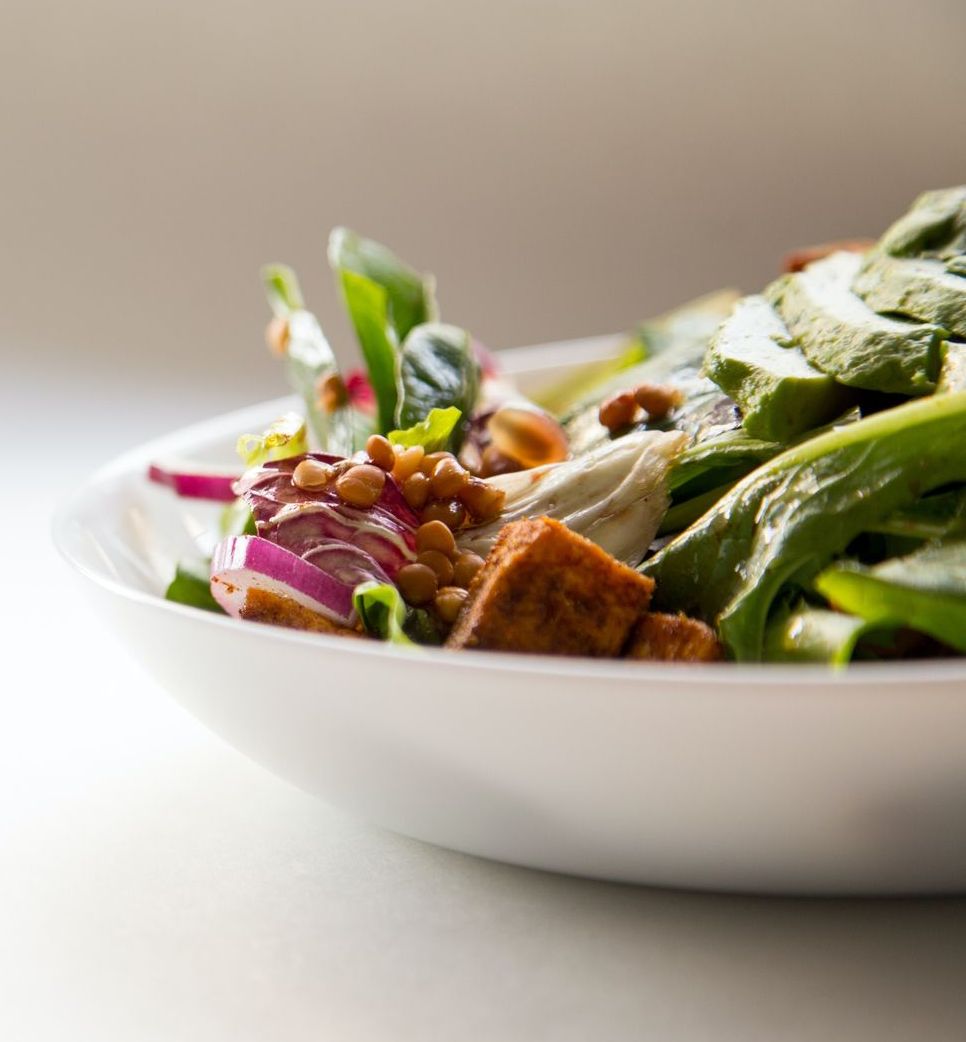 A white bowl overflowing with a fresh salad; featuring spinach, red onion, and toasted nuts.
