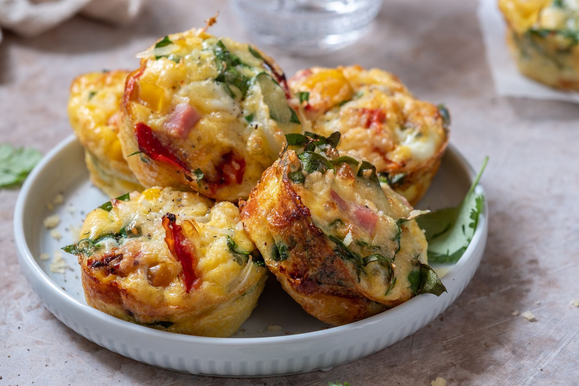 Savory egg muffins with vegetables and bacon on a white plate, set on a neutral surface.