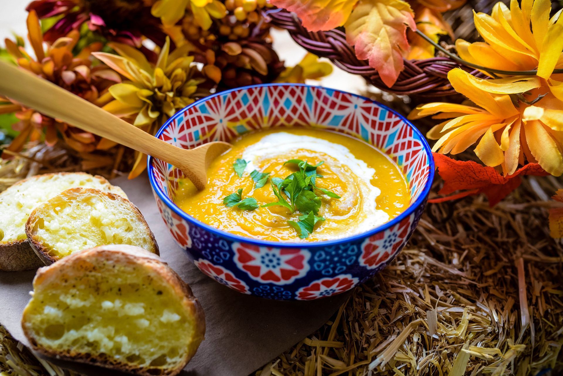 Bowl of orange soup with cream and garnish, served with garlic bread, surrounded by autumn decorations.