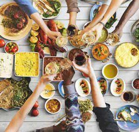 People clink glasses around a table laden with various dishes, including a lobster, pasta, and appetizers.