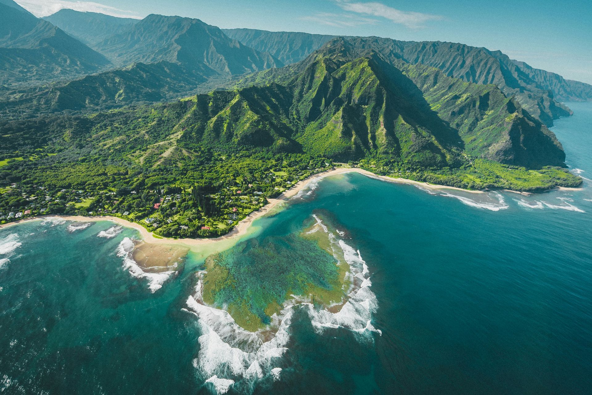 Coastal mountain landscape with lush green vegetation, turquoise ocean, and a small beach area.