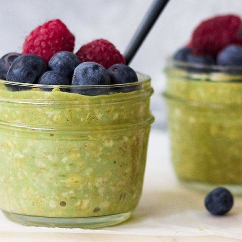 Two glass jars filled with green oatmeal, topped with blueberries and raspberries.