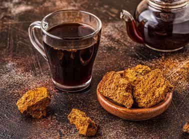 A cup of dark tea, a teapot, and chunks of chaga mushroom in a wooden bowl on a textured surface.