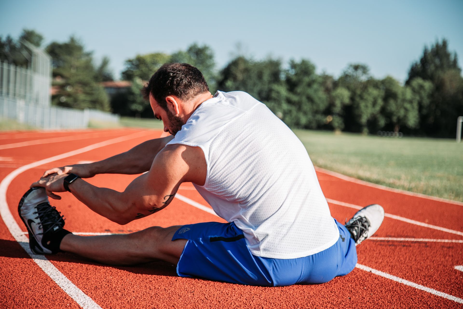A man in athletic wear stretches his legs on a red track. He is reaching for his toes.