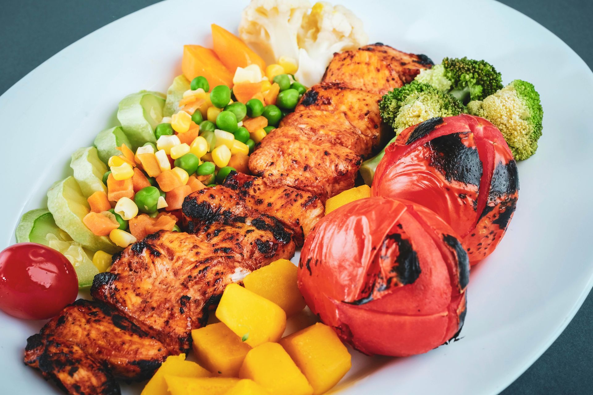 Grilled chicken kebab with assorted grilled vegetables and sides on a white plate.
