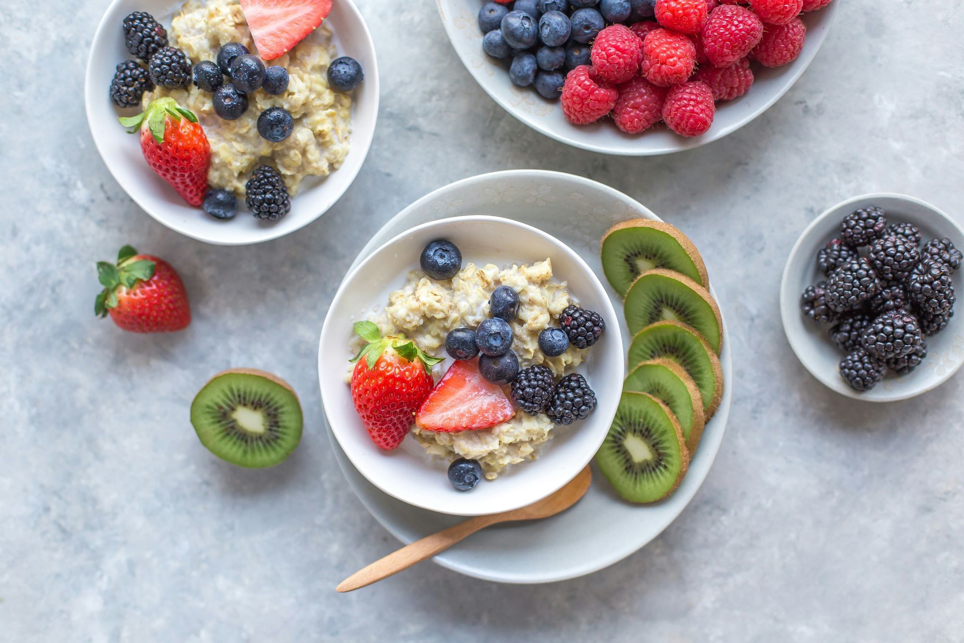 Oatmeal bowls topped with berries and sliced kiwi on a light-colored surface. A bowl of mixed berries sits nearby.