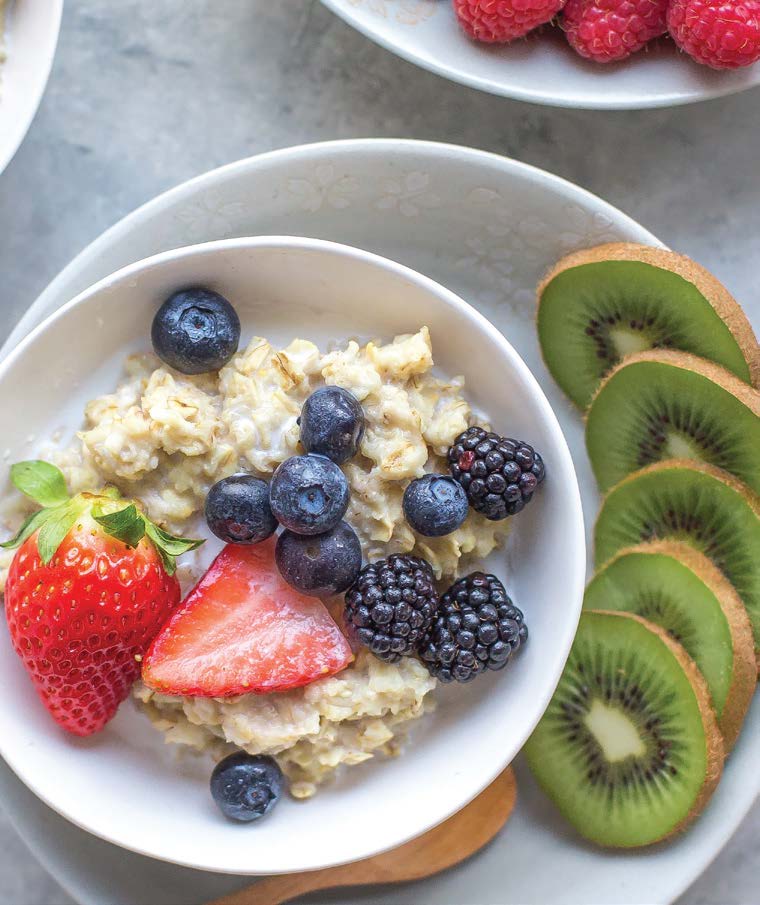 Oatmeal with berries (strawberries, blueberries, blackberries) and kiwi slices on a white plate.