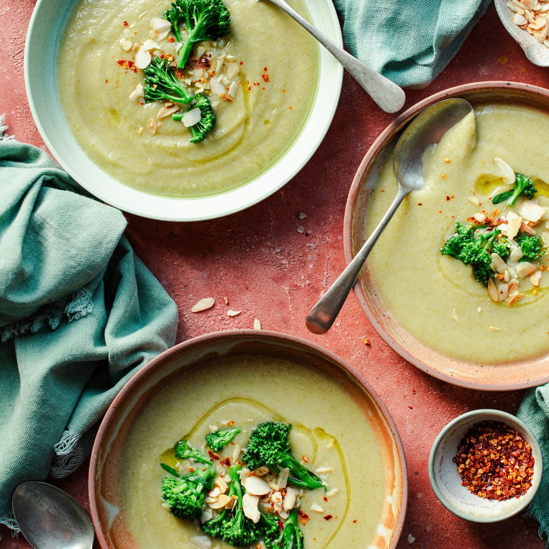 Three bowls of green broccoli soup, garnished with broccoli florets and almonds.