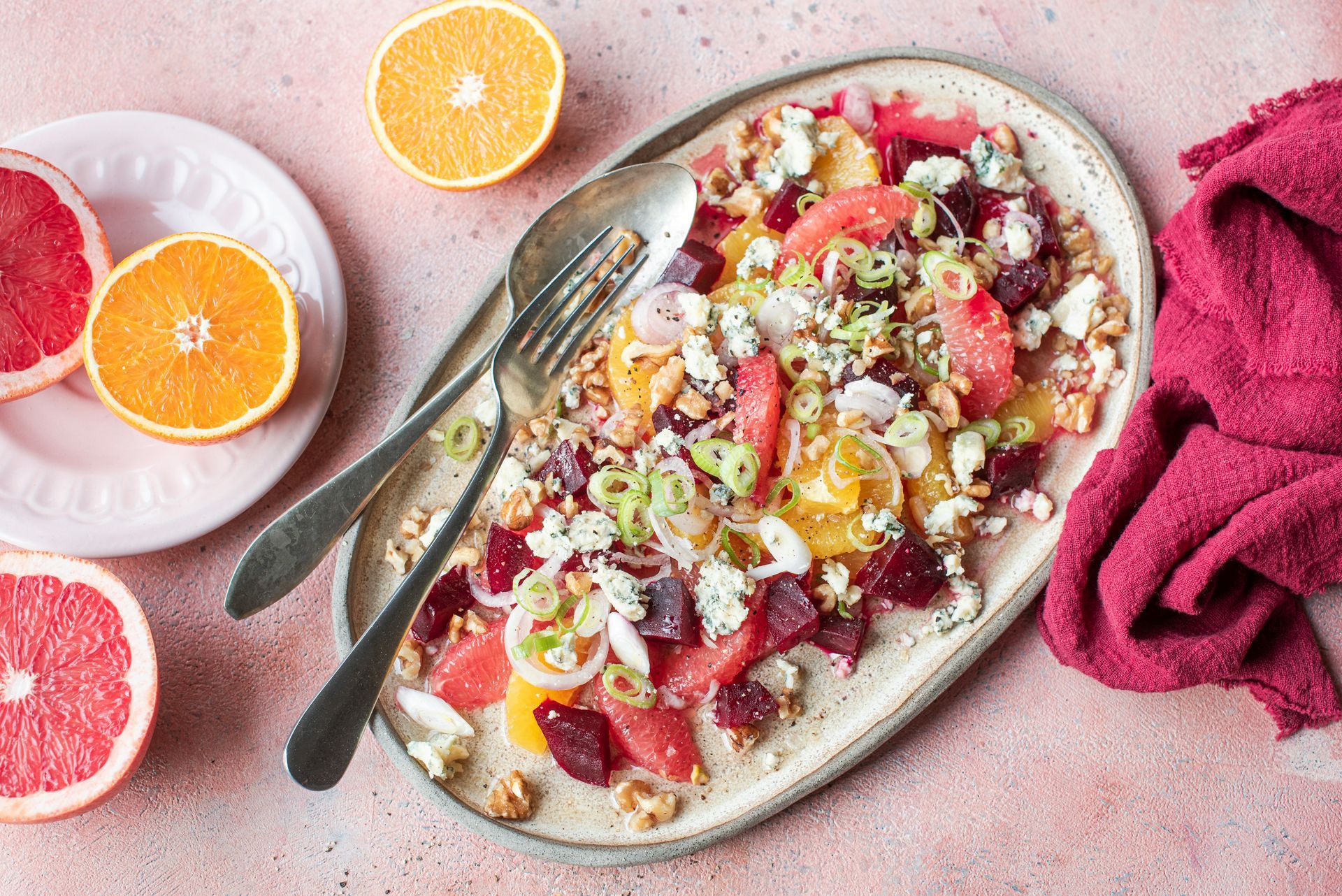 Citrus salad with grapefruit, oranges, beets, and walnuts, garnished with green onions and feta, served on a platter.