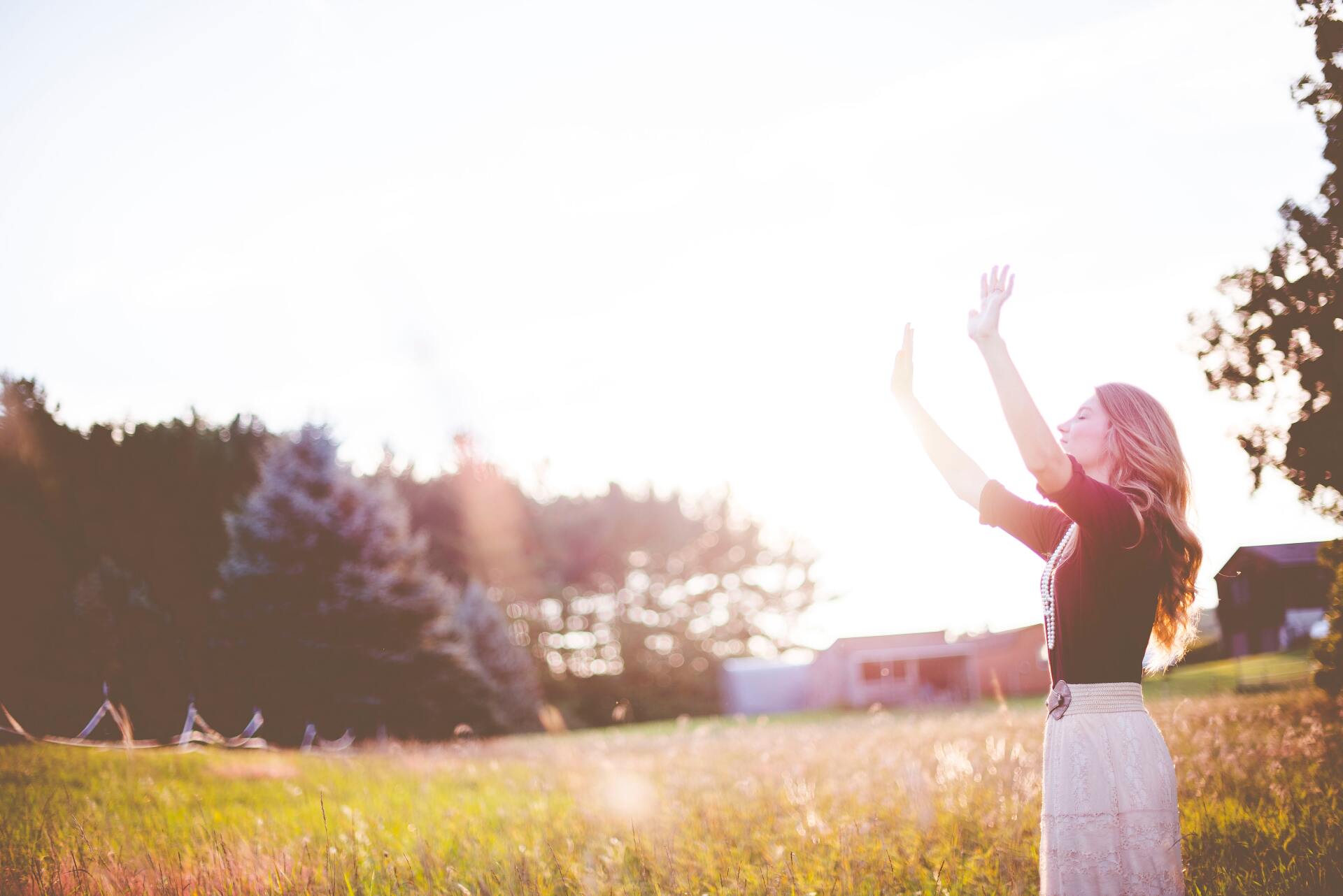 Woman in a field raises her arms towards the bright sun. Warm, golden light bathes the scene.