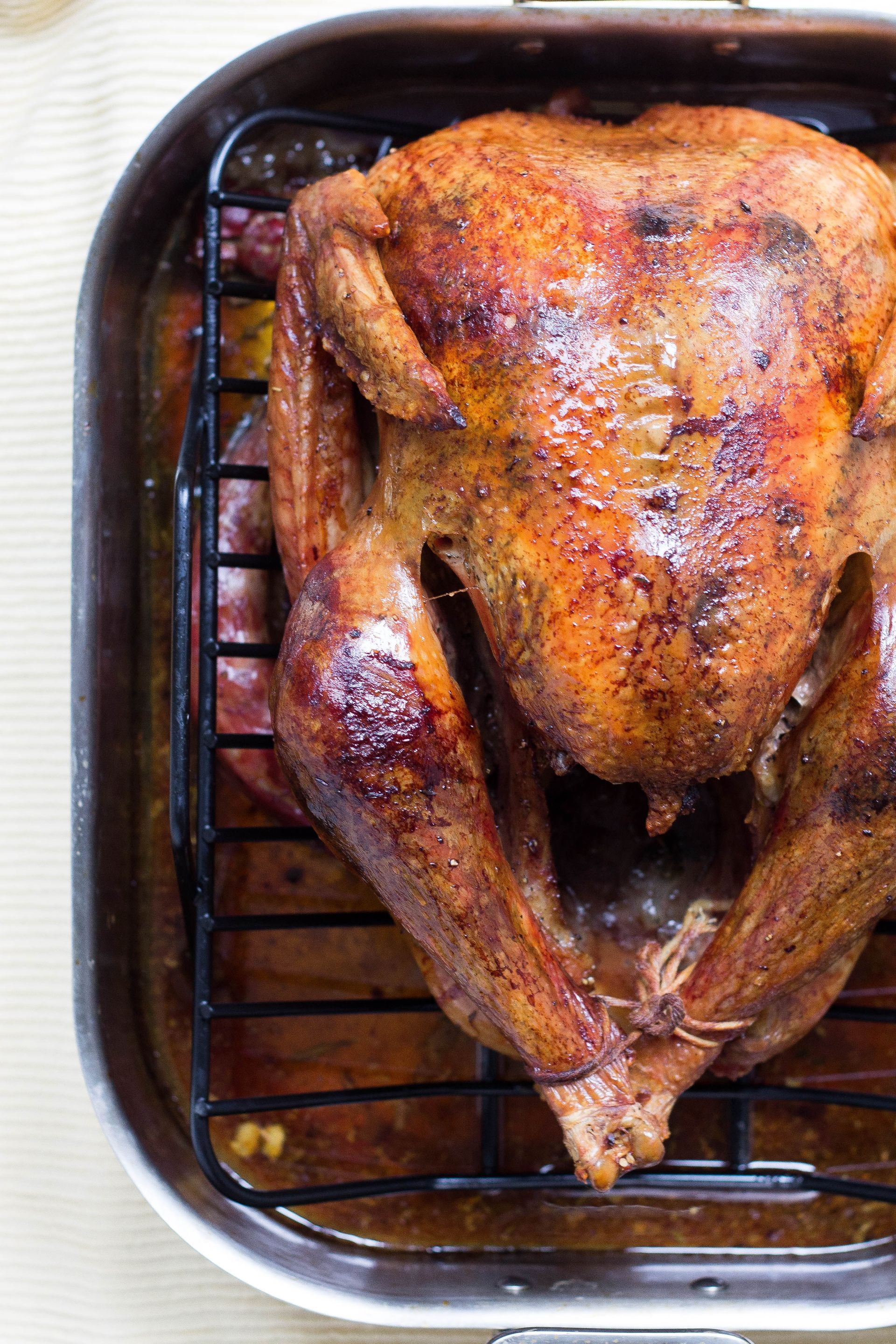 Roasted turkey in a metal roasting pan, golden brown skin, sitting on a black rack, with brown juices.