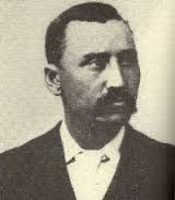 A black-and-white portrait of a man with a mustache wearing a suit and tie.