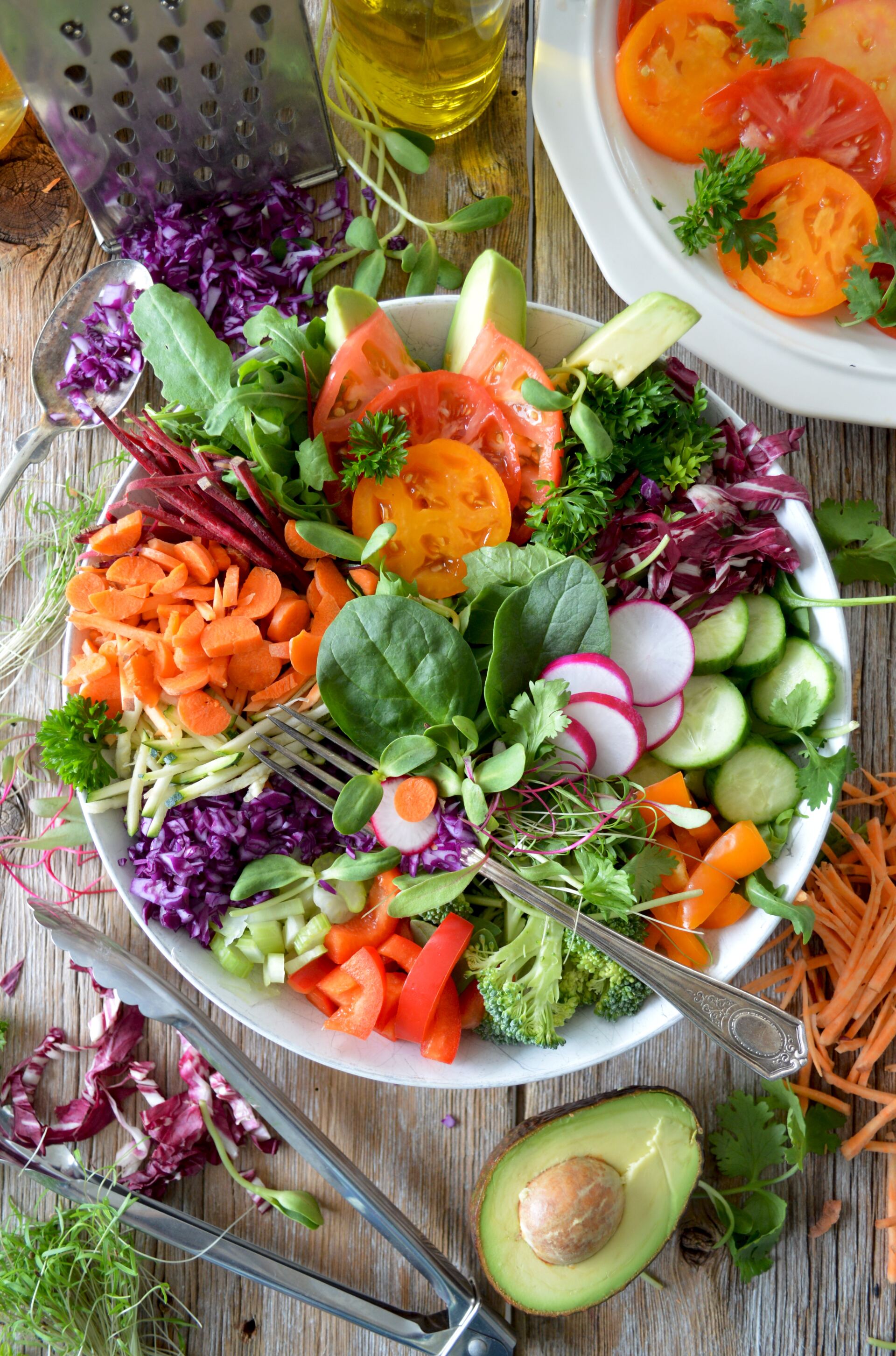 Colorful vegetable salad in a white bowl with tomatoes, avocado, and greens on a wooden table.