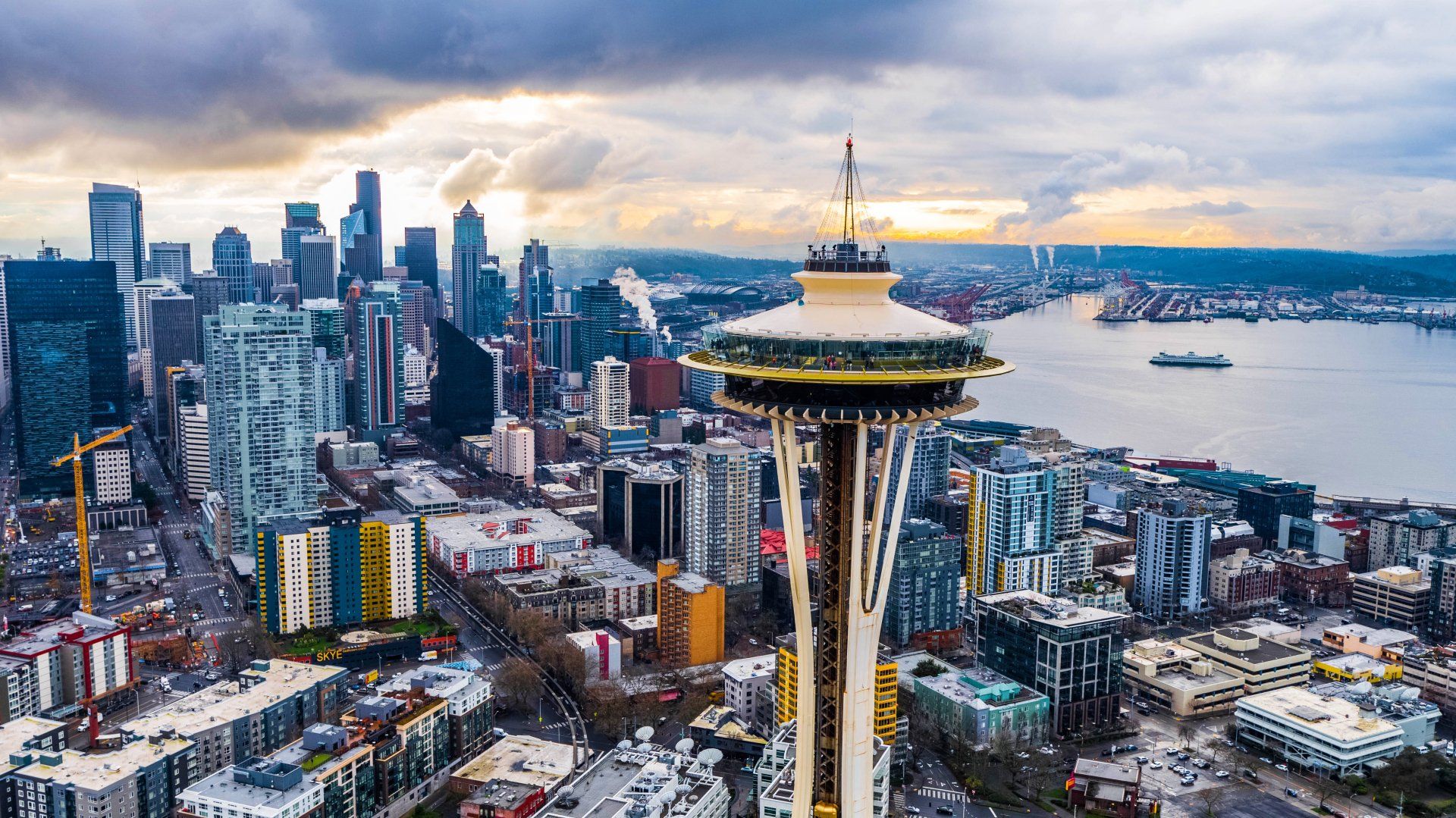 Seattle skyline with Space Needle prominent, under a cloudy sky, near the waterfront.