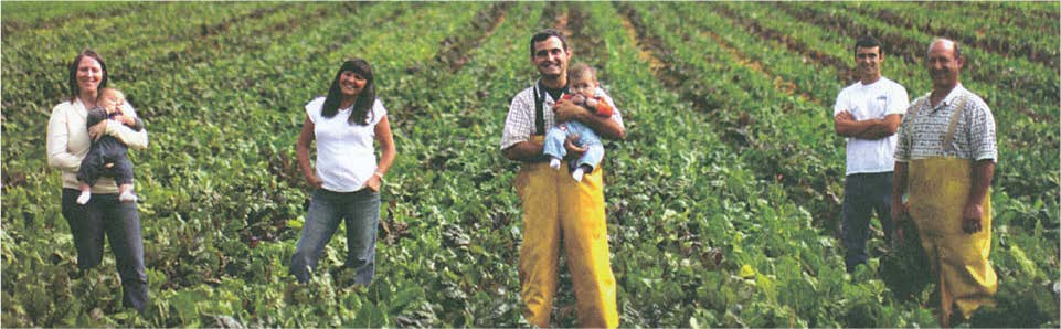 Five people stand in a field of green plants. Two women each hold a baby, while the other three men look at the camera.