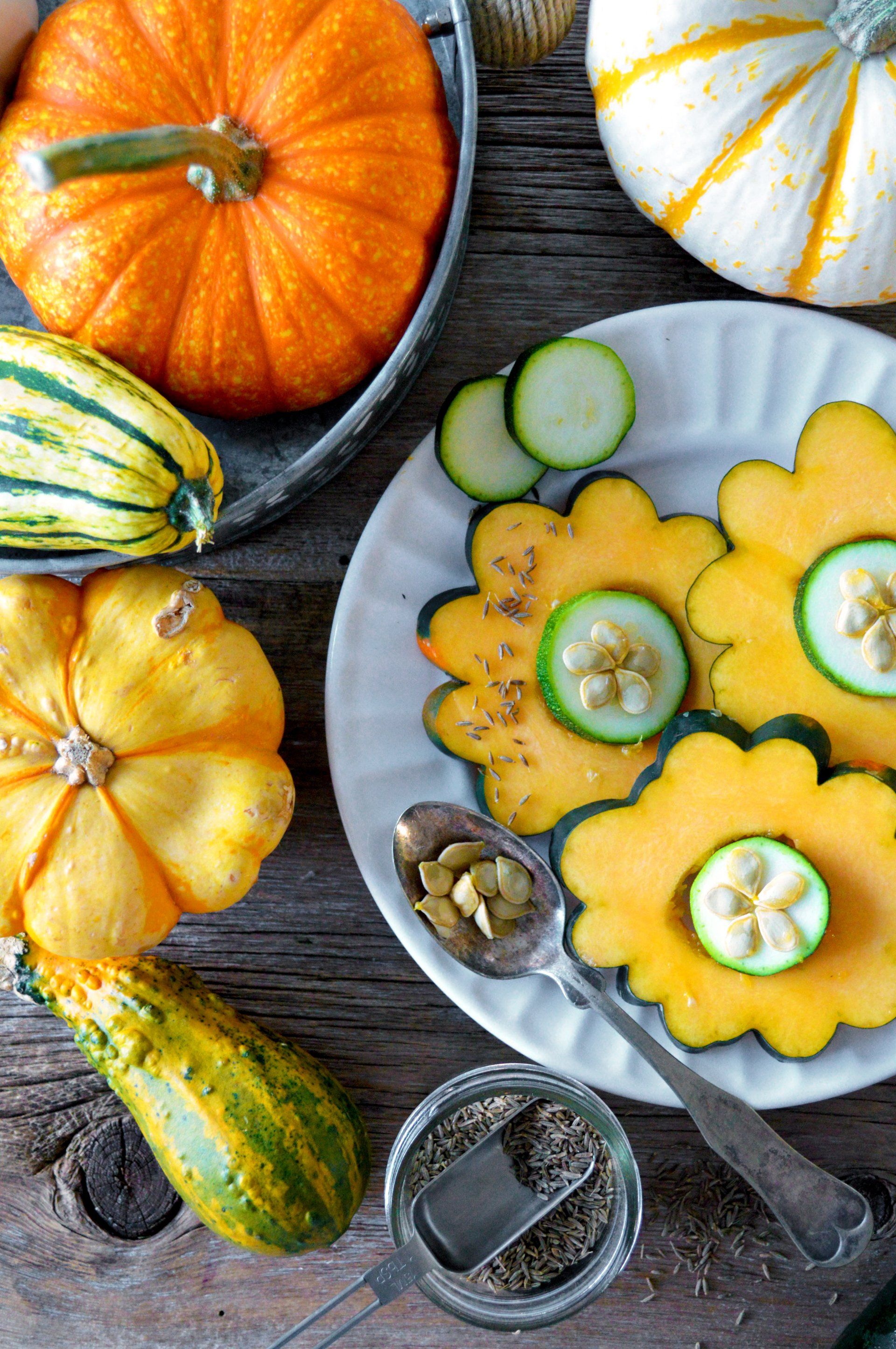 An overhead shot of fall squash and zucchini slices on a plate with spice and pumpkins on a wooden table.