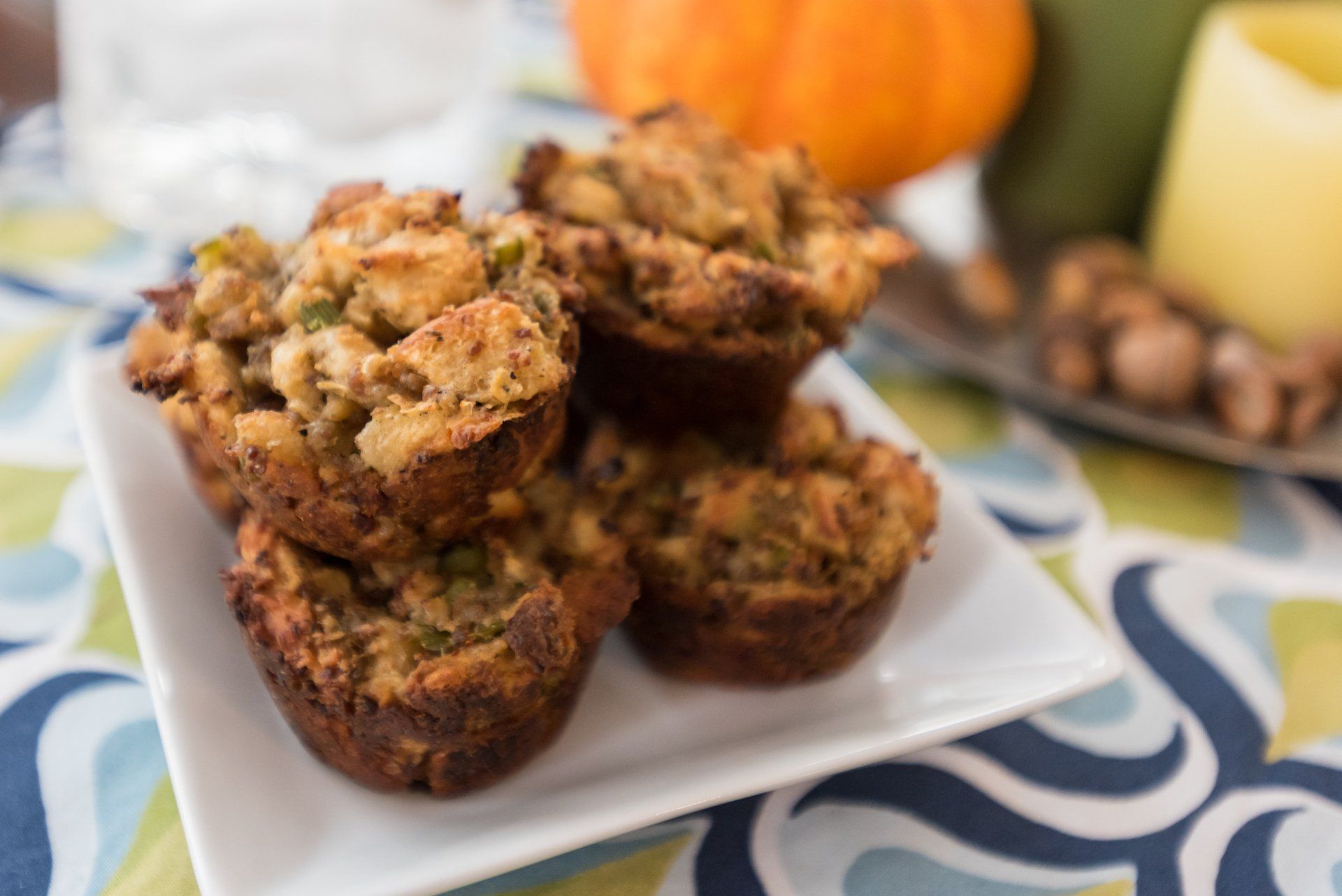 A white plate holds a stack of browned stuffing muffins; a small pumpkin and candle are in the background.
