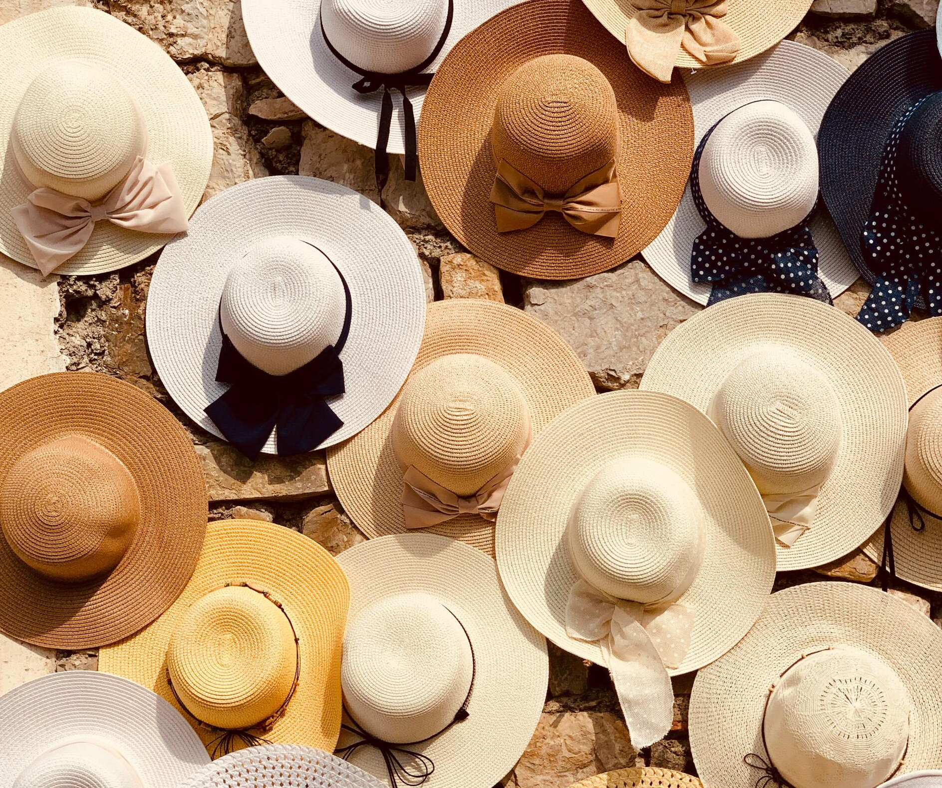 A collection of sun hats of various colors and styles, including straw and ribbon details, arranged on a wall.