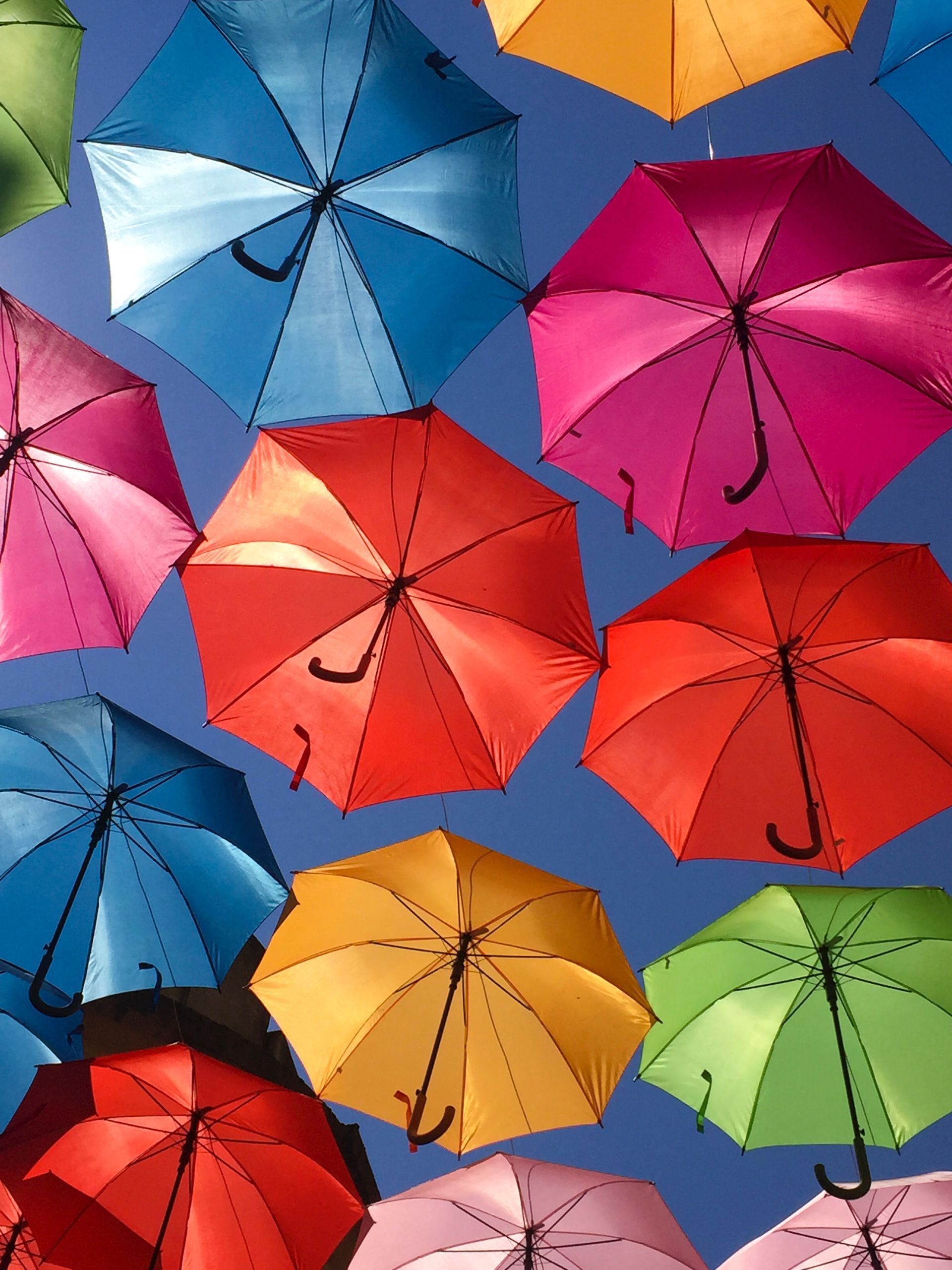 Brightly colored open umbrellas suspended in the air against a clear blue sky.