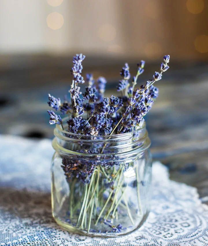 Lavender sprigs in a clear glass jar sit on a blue and white patterned surface.
