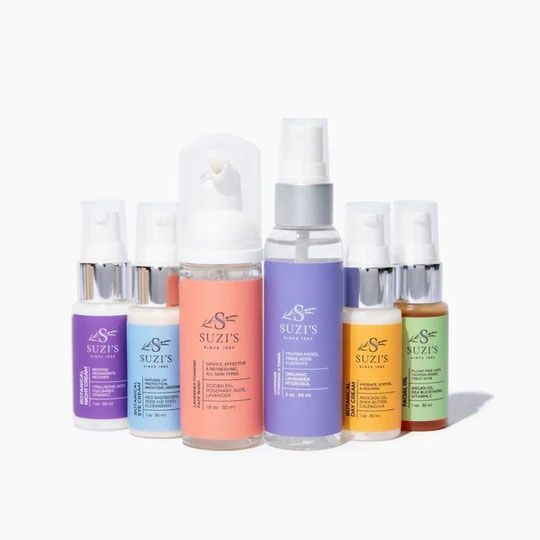 Collection of Suzi's skin care products in various bottles, featuring colorful labels and silver pumps, on a white background.