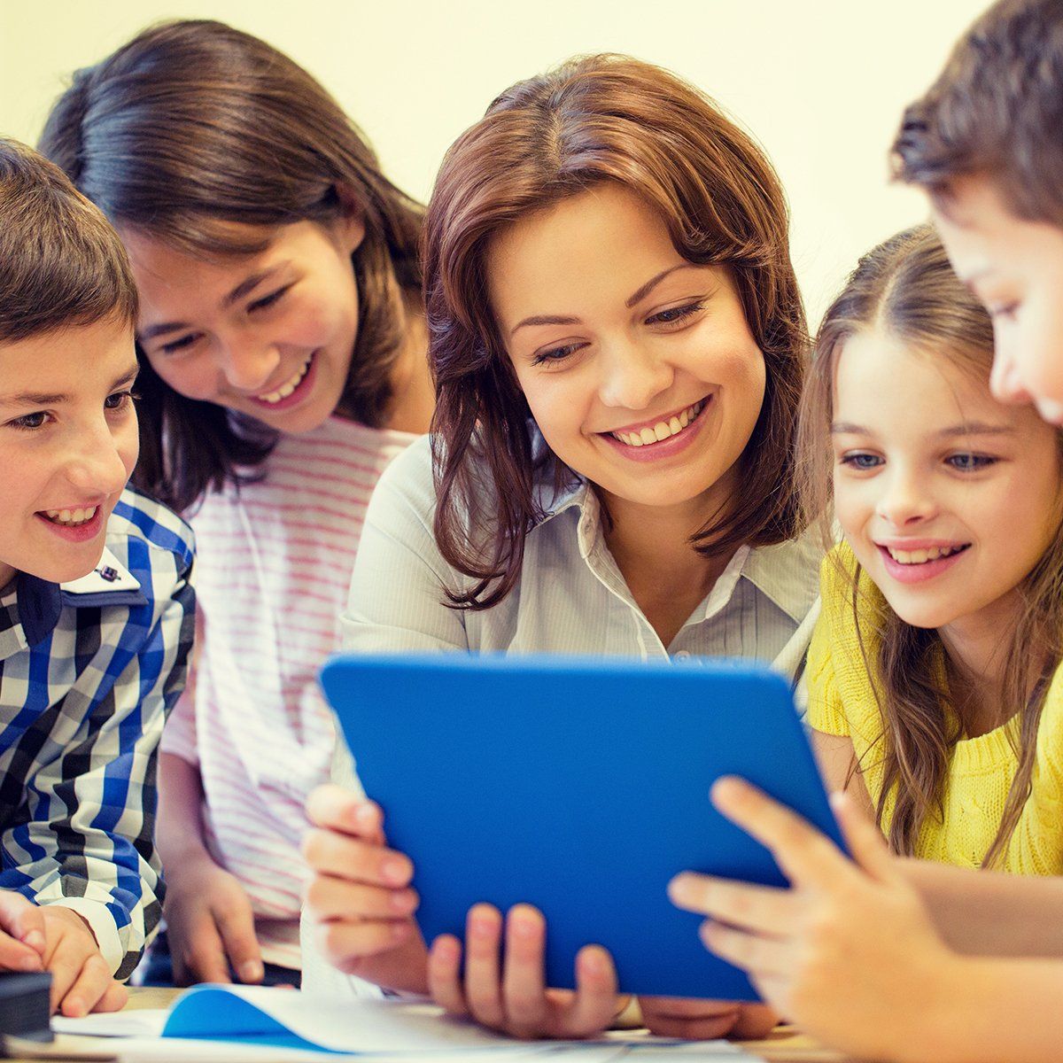 A teacher and children smiling while looking at a blue tablet. They are in a classroom setting.
