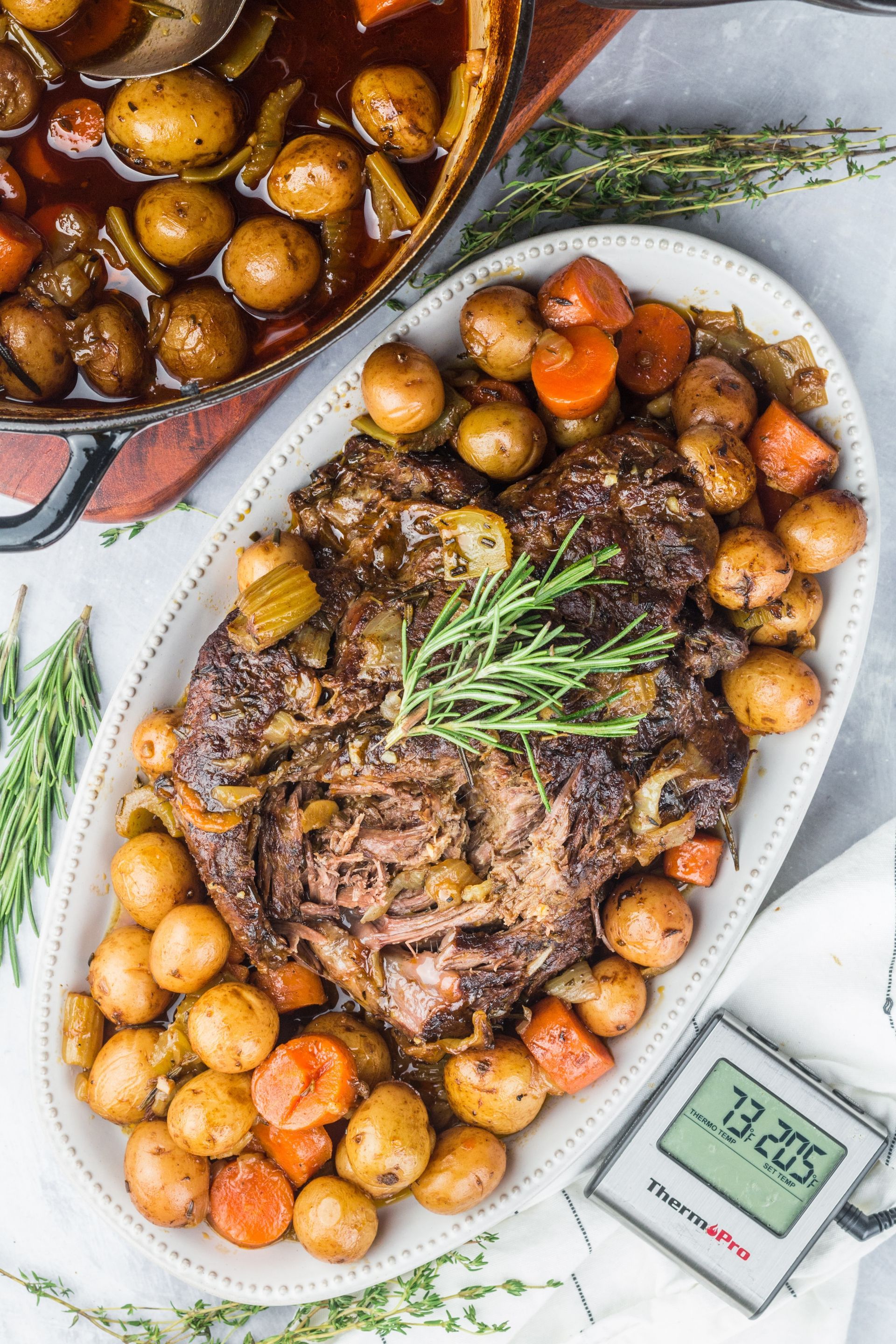 Oval platter with cooked pot roast, baby potatoes, carrots, and rosemary. A Thermapen thermometer rests on the platter's edge.