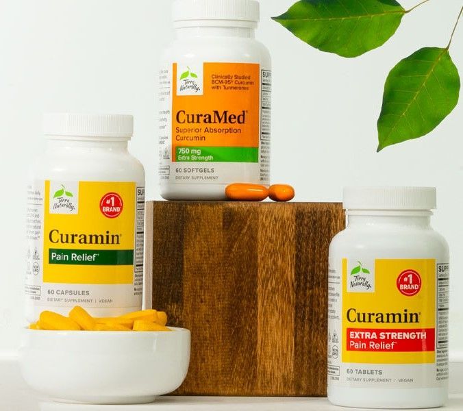 Three white bottles of supplements with orange and yellow pills in a studio setting, with leaves in the background.