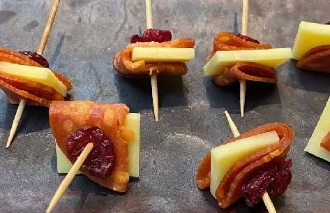 Skewers with cheese, pepperoni, and dried cranberries on a dark surface. Each skewer has a cube of cheese, slices of pepperoni, and a cranberry.