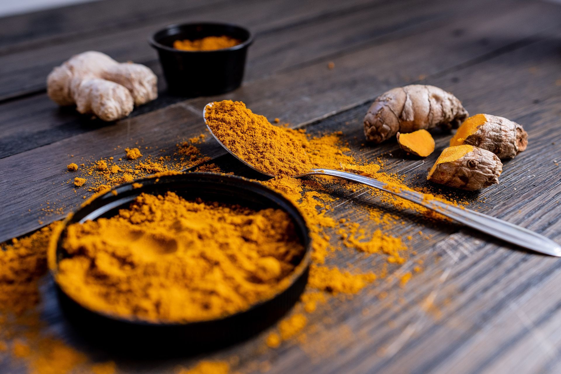 Turmeric spice and roots on a wooden surface, with a spoon scooping yellow powder.