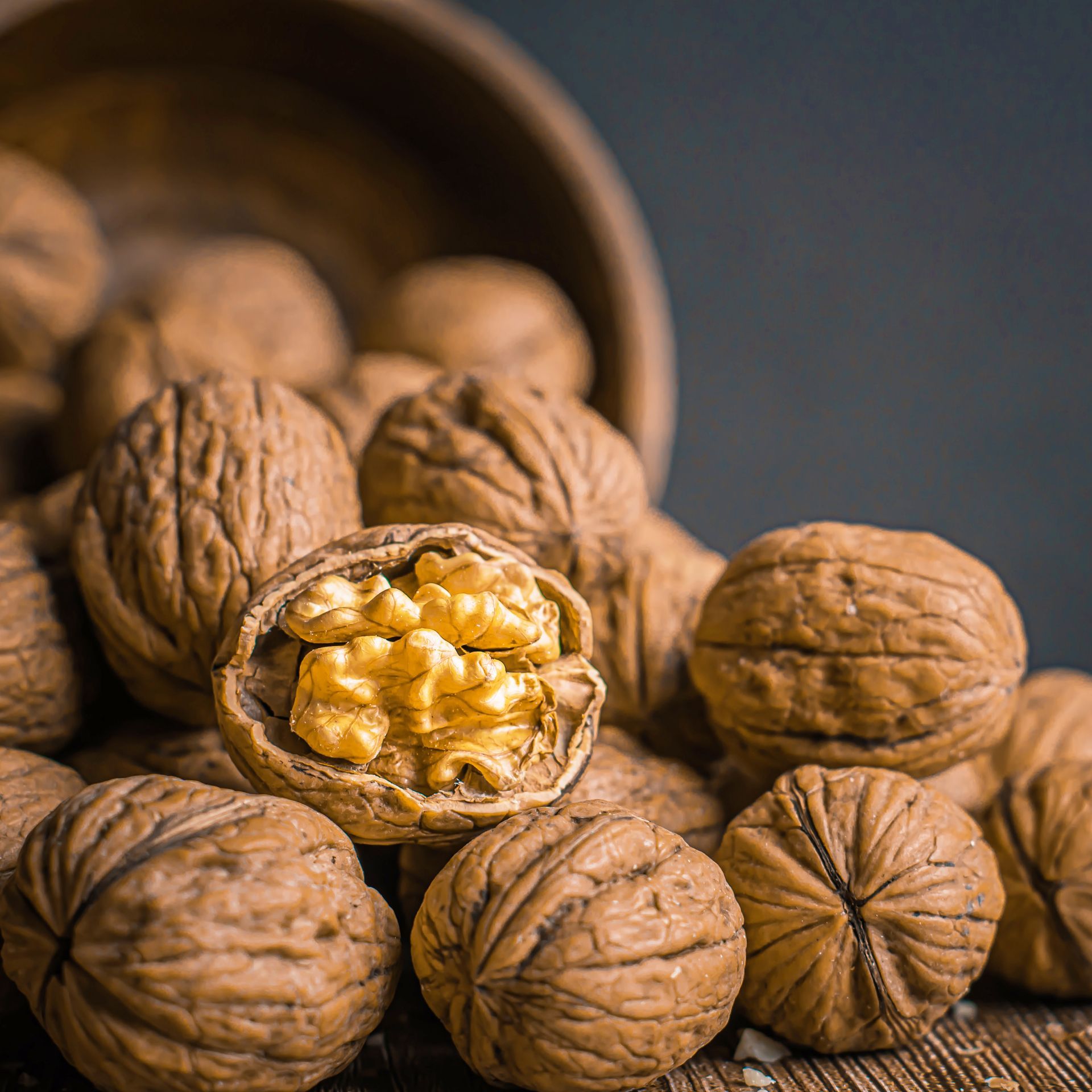 Walnuts spilling from a wooden bowl. One is cracked open, revealing a golden nut meat.