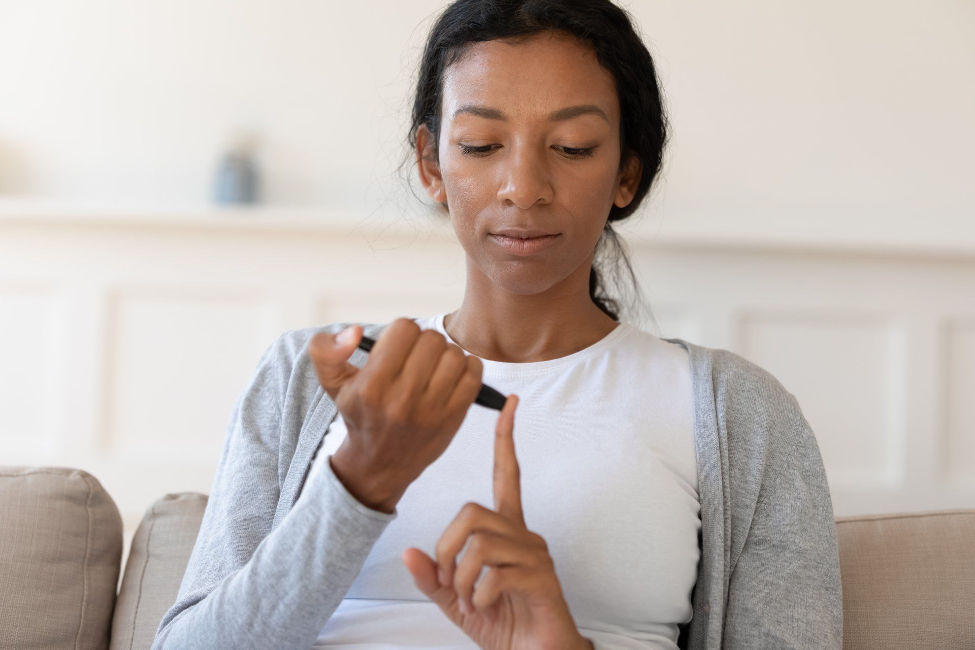 Woman checking blood glucose, using a lancet on her finger indoors. She is looking down with a focused expression.