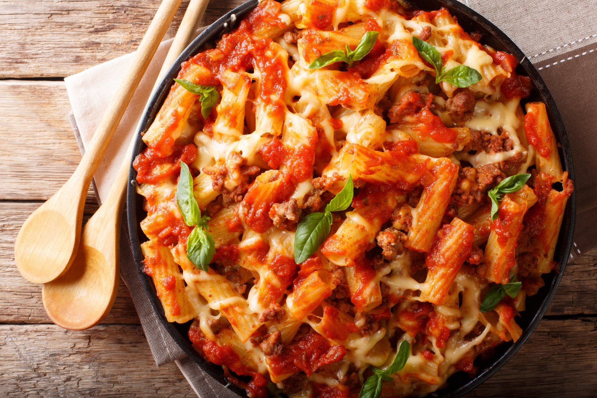 Baked pasta dish with rigatoni, tomato sauce, ground meat, and melted cheese, garnished with basil.