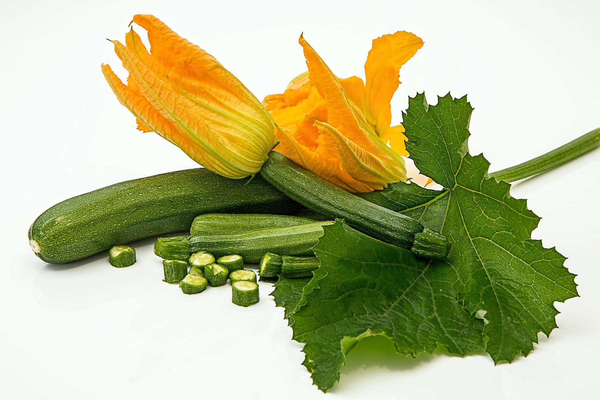 Zucchini with bright yellow blossoms, green leaves, and chopped pieces on a white surface.